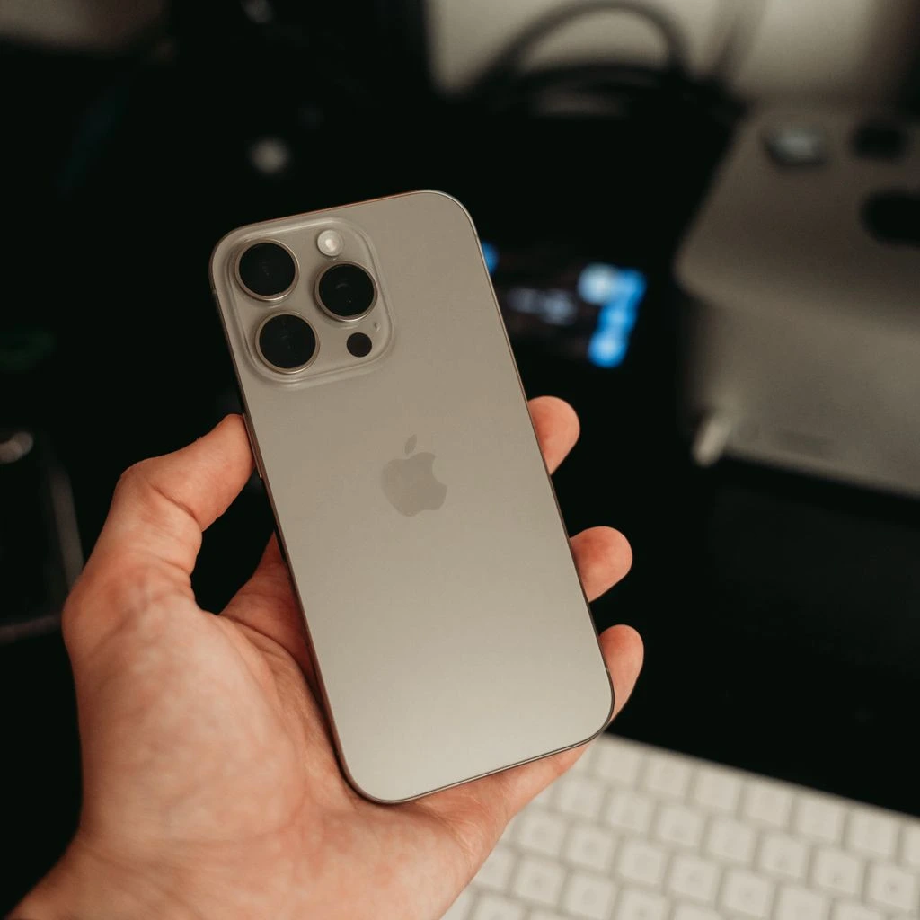 iPhone 16 Pro Max in natural titanium, resting flat on a slate surface.